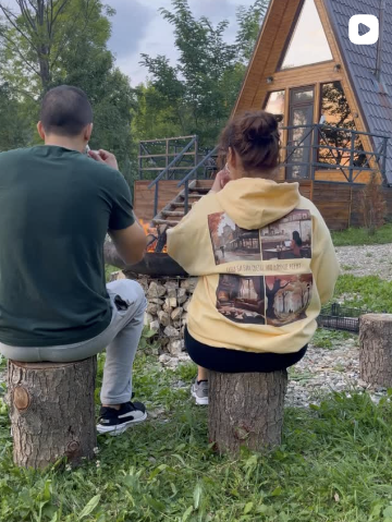 Two people sitting on tree stumps in a backyard with a small cabin in the background.